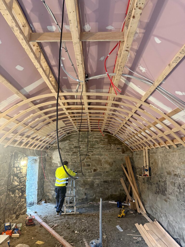 Electrician on a ladder doing the first fix wiring under the new ceiling frame at Fagan’s temporary bar, Moynalvey
